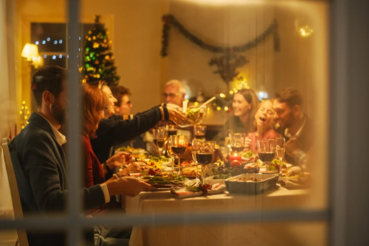 Zdjęcie okna za którym siedzi rodzina przy wigilijnym stole.