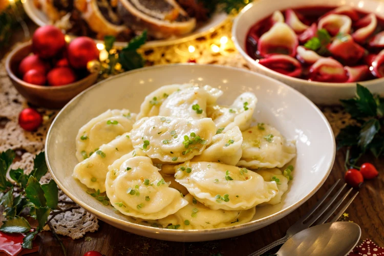 Zdjęcie pierogów, barszczu czerwonego z uszkami oraz makowca na wigilijnym stole.