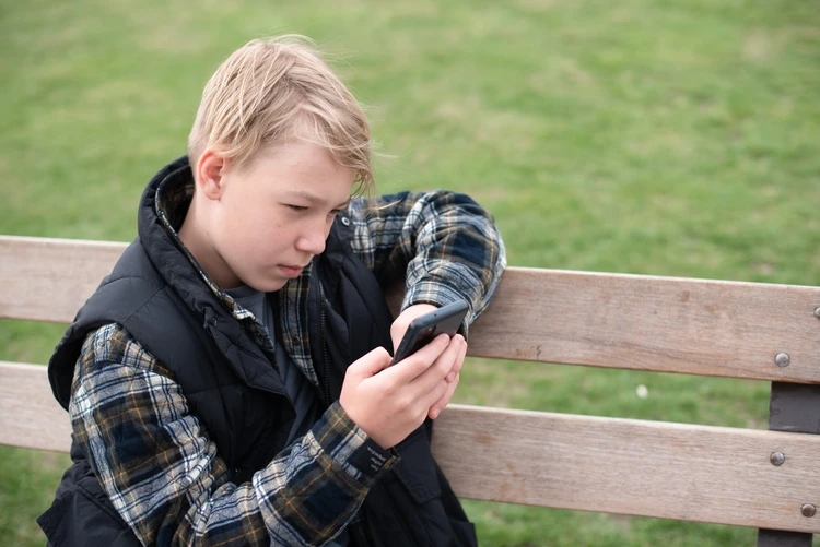 Chłopiec na ławce patrzący w ekran telefonu