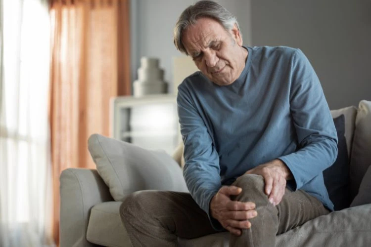 Zdjęcie starszego mężczyzny, który siedzi na kanapie i trzyma się za kolano