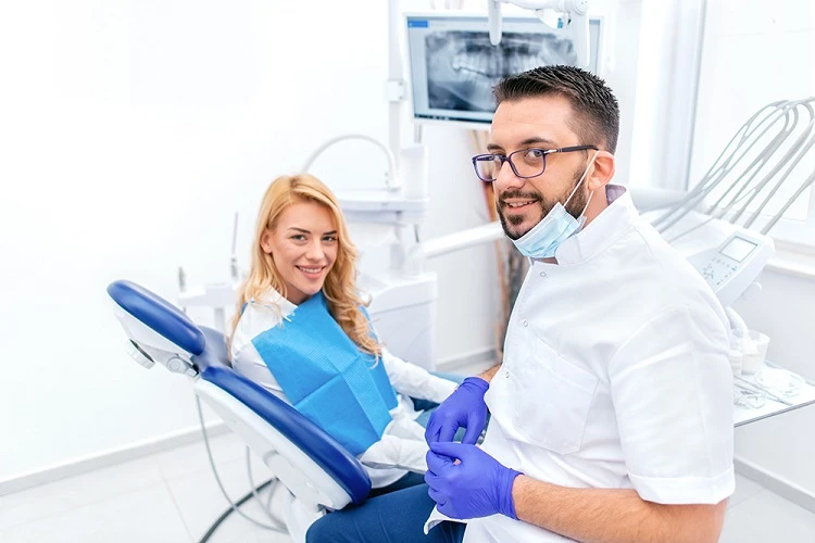 Lekarz stomatolog w gabinecie obok siedzącej na fotelu pacjentki