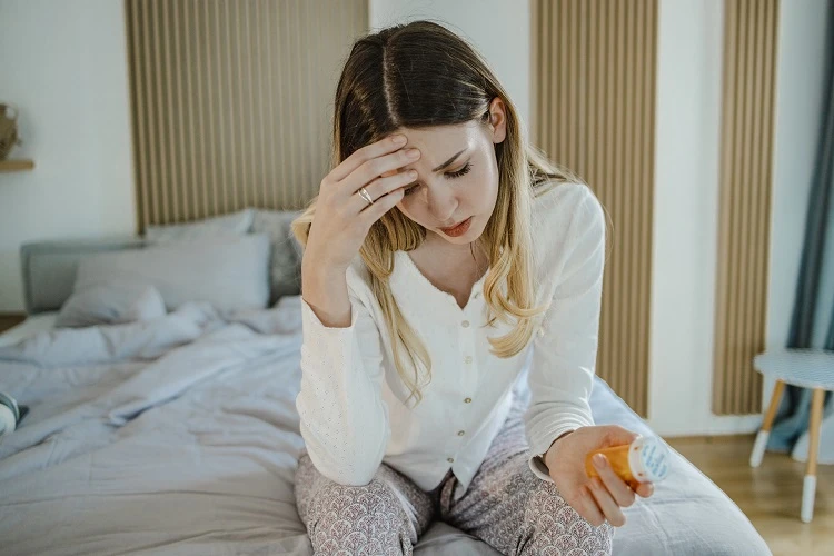 Młoda kobieta siedzi na łóżku i trzyma w dłoni buteleczkę leków