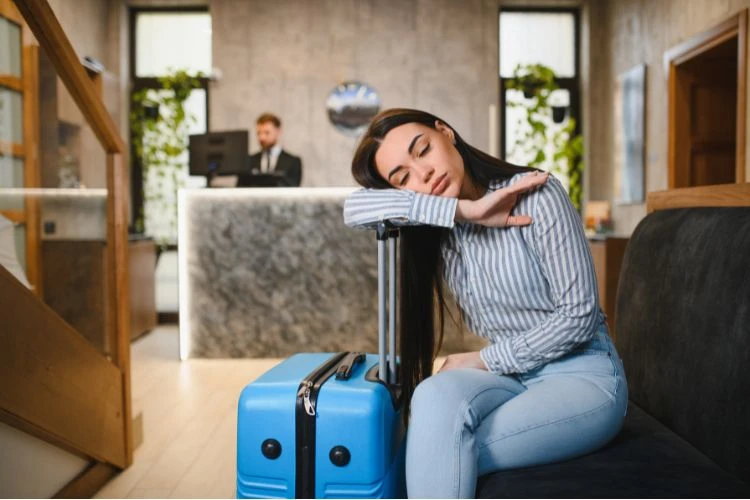 Zdjęcie kobiety przysypiającej z walizką w lobby hotelu.