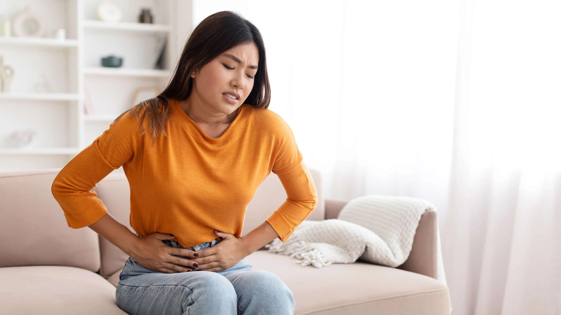 Kobieta z grymasem na twarzy trzyma się za brzuch