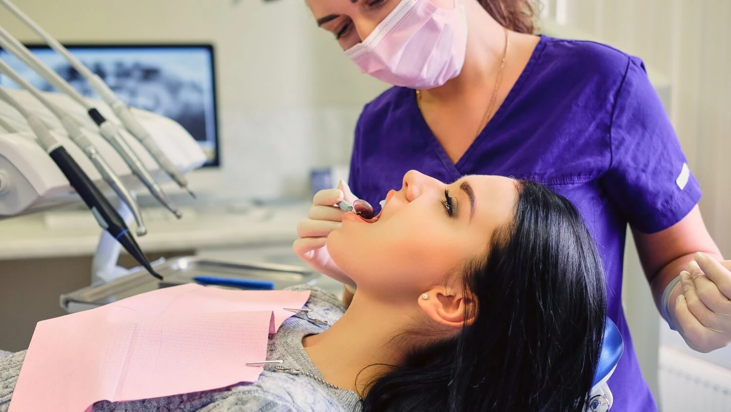 Stomatolog wykonuje zabieg higienizacji zębów u młodej kobiety na fotelu dentystycznym