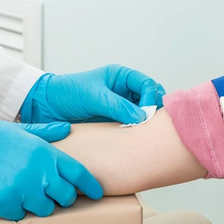 Dłonie pracownika medycznego przygotowują rękę pacjenta do pobrania krwi