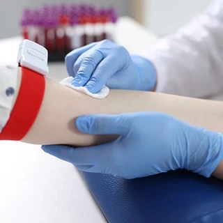 Dłonie pracownika medycznego przygotowują rękę pacjenta do pobrania krwi