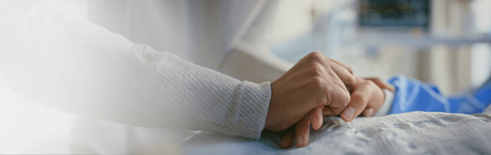 Dłoń kobiety trzymająca dłoń osoby leżącej na szpitalnym łóżku