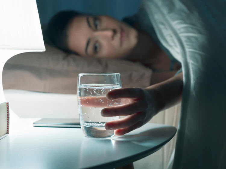 Kobieta sięgająca po szklankę wody w nocy