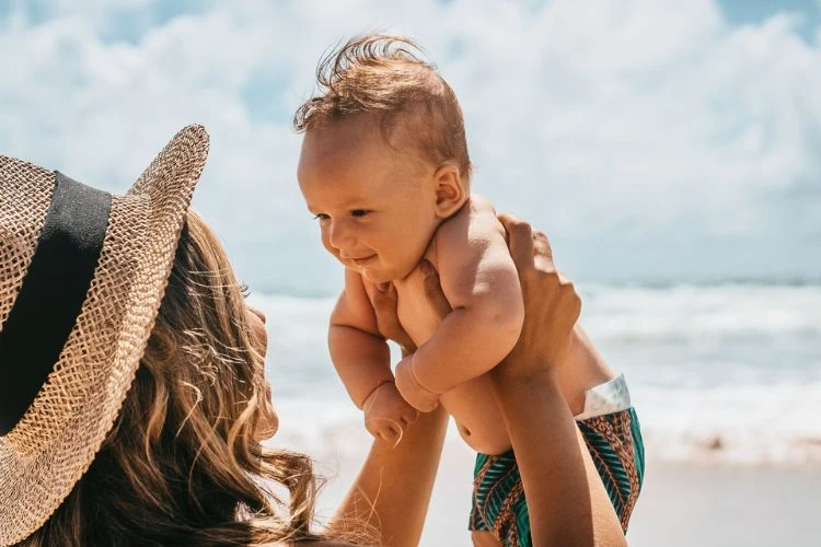 Zdjęcie niemowlaka trzymanego na rękach mamy na plaży.