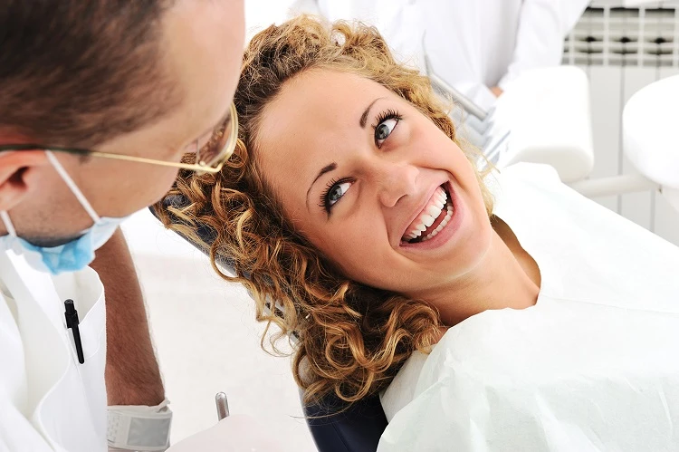 Kobieta siedzi na fotelu dentystycznym i uśmiecha się do lekarza